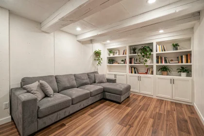 Sous-sol transformé en salon confortable avec canapé gris, parquet stratifié et murs en béton peint blanc